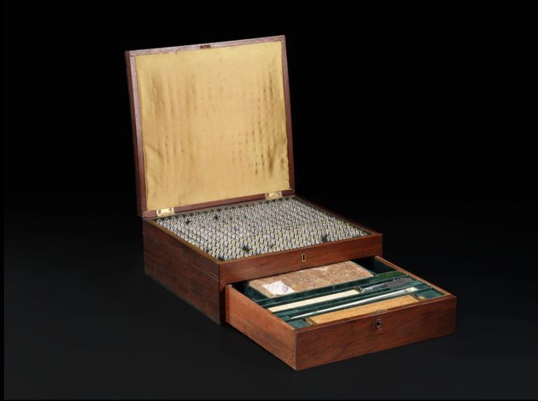A wooden box filled with glass beads, photographed against a black background.