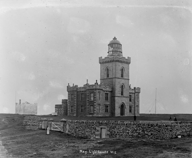 A black and white image of a lighthouse situated in a field with a stone wall enclosing it