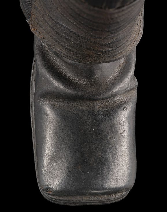 Detail of jack boot showing square toes propped up against a black background.