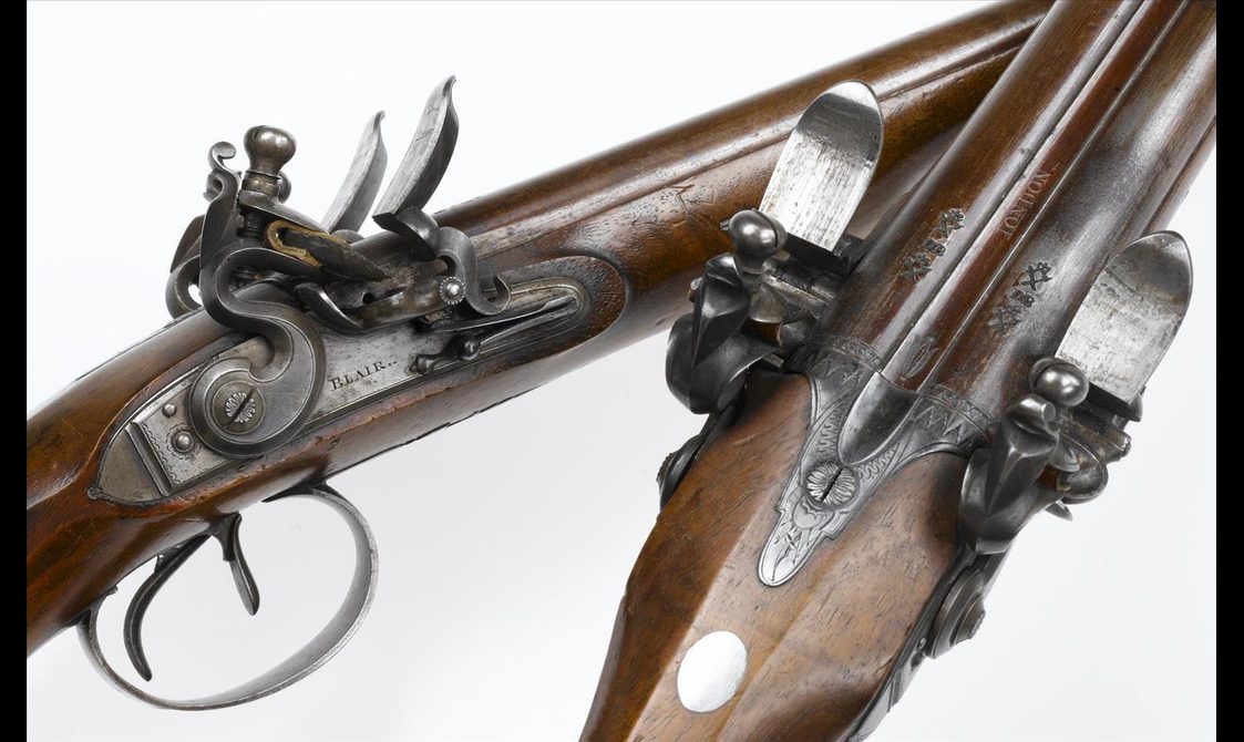 A close up of two wooden pistols, showing the intricate metal detail of the mechanism.