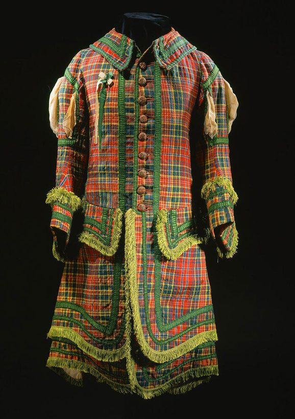 A red, green and yellow tartan knee length uniform jacket with green ruffles and a yellow green ribbon pinned to the left side of the chest. set against black background.