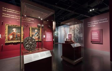 Two museum cases in the Bonnie Prince Charlie and the Jacobites exhibition. In the left case is a circular shield and in the right case is a collection of silverware.