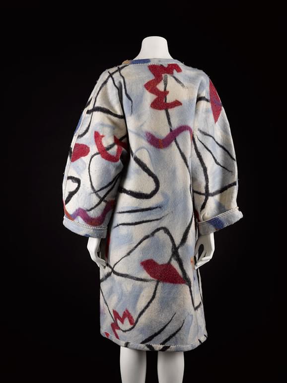 A back view of a mannequin wearing a grey wool felt coat with red, blue, and black abstract line patterns