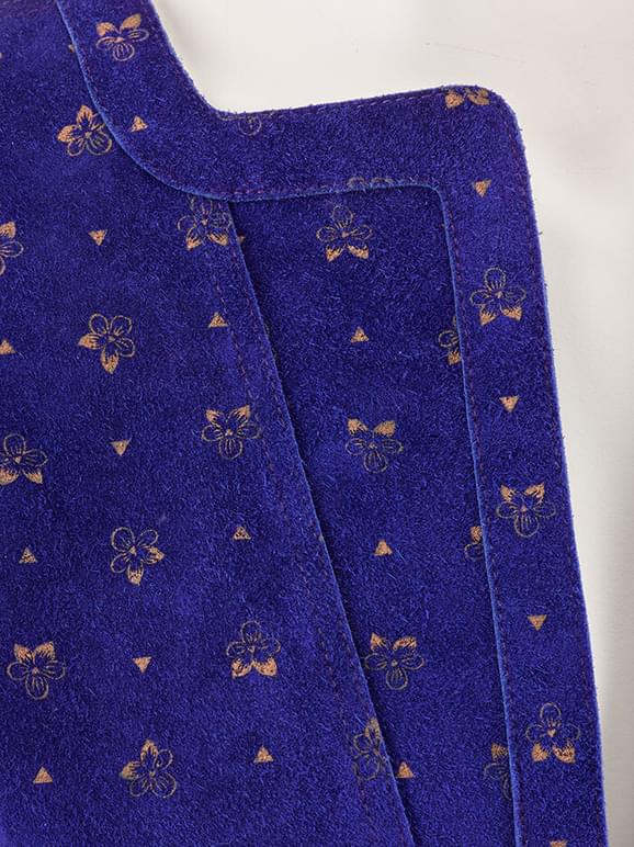 Detail of a royal blue suede top with a gold floral print.