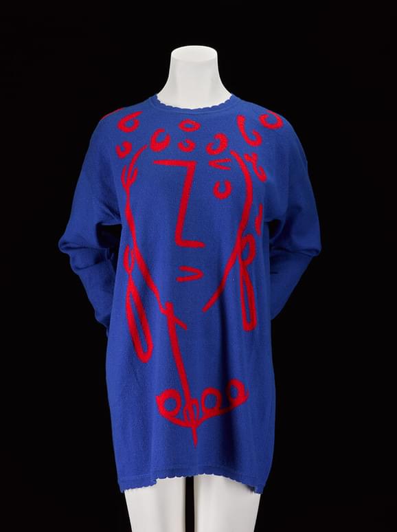 A mannequin wearing a long blue jumper with a red abstract print of a face.