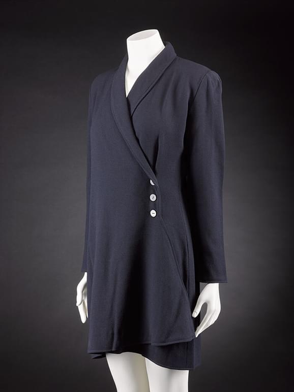 A mannequin wearing a navy wool crepe coat that fastens to the left with three buttons.