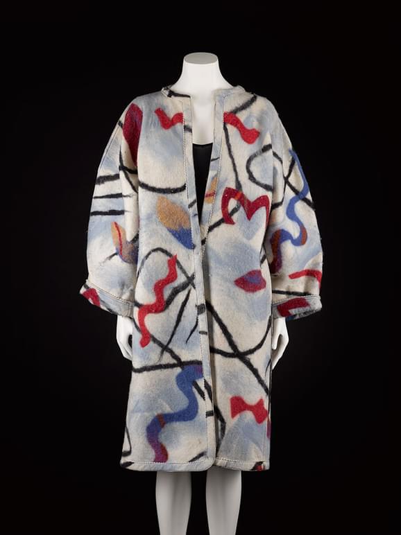 A mannequin wearing a grey wool felt coat with red, blue, and black abstract line patterns