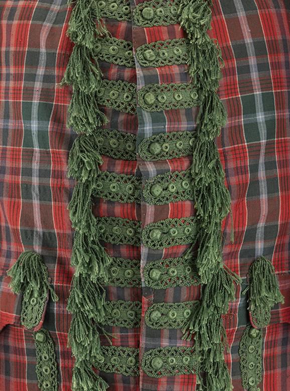A close up of a red and green tartan jacket. Elaborate green embroidery and tufts are placed around the green buttons in the center of the jacket.