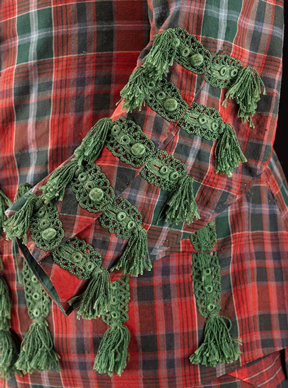 A close up of a green and red tartan suit sleeve. The buttons off the sleeve are decorated with elaborate green embroidery and tufts.
