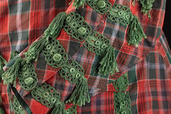 A close up of a green and red tartan suit sleeve. The buttons off the sleeve are decorated with elaborate green embroidery and tufts.