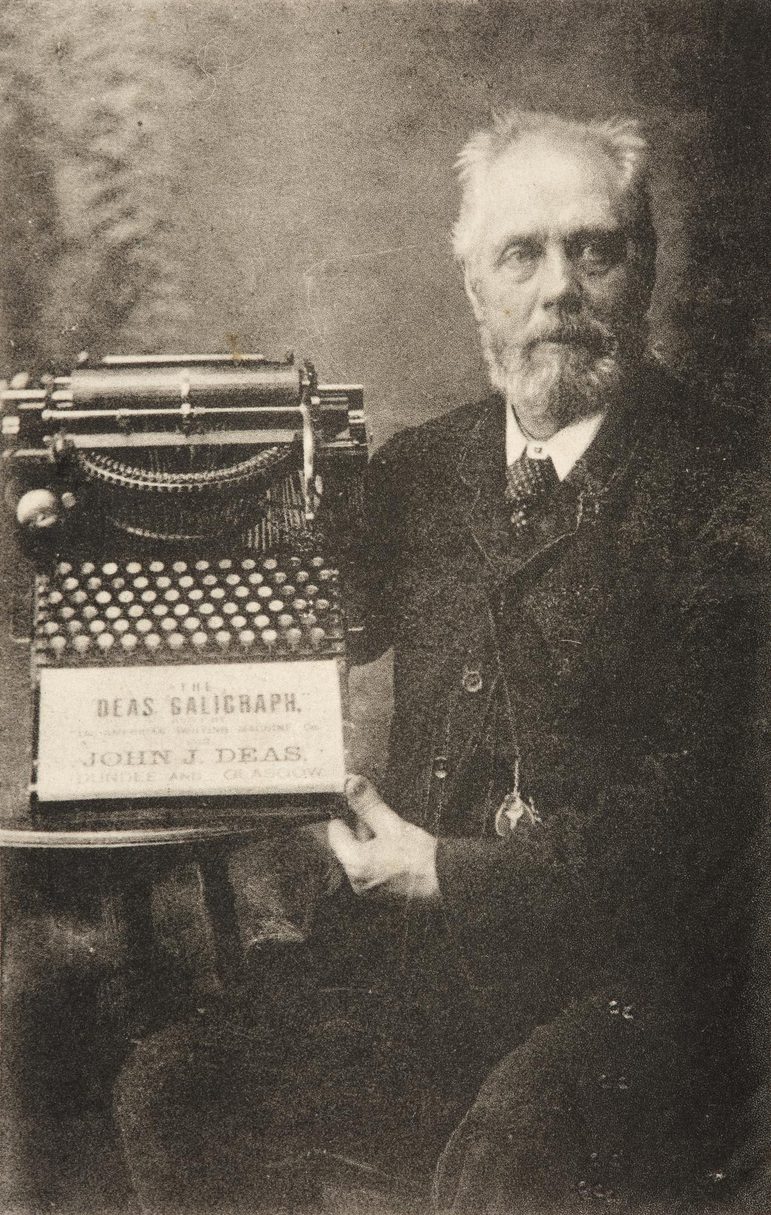 A black and white photograph of a man in a suit holding a typewriter