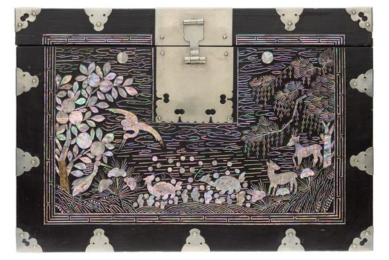 The top of a black bock with pearl embellishments depicting trees, birds, and animals. There is a large latch or hinge in the top middle.