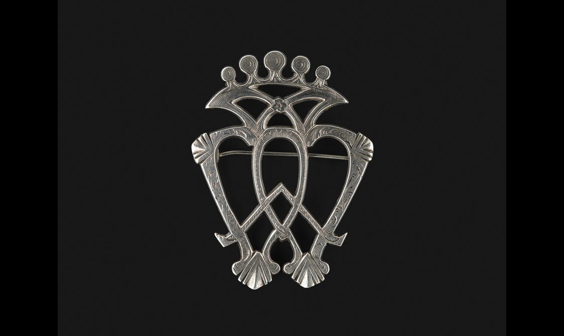 Detail of a silver heart brooch, highlighting the criss-crossed bars and crown-like top section.