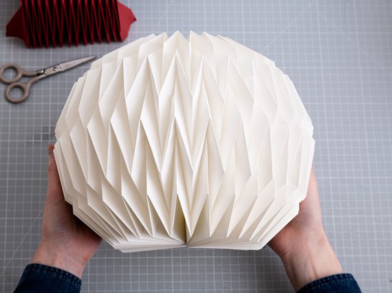 A paper of hands hold a folded bit of paper with diagonal patterns.