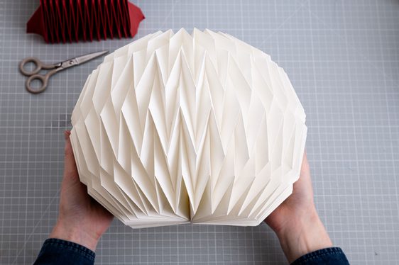 A paper of hands hold a folded bit of paper with diagonal patterns.