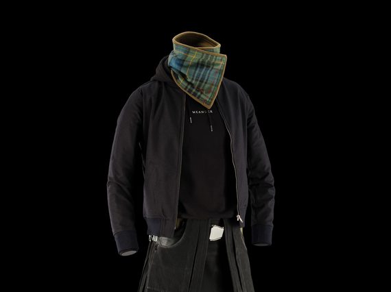 A mannequin wearing a black denim kilt, a black hoodie, a black jacket, and a green and blue tartan neck scarf.
