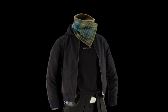 A mannequin wearing a black denim kilt, a black hoodie, a black jacket, and a green and blue tartan neck scarf.