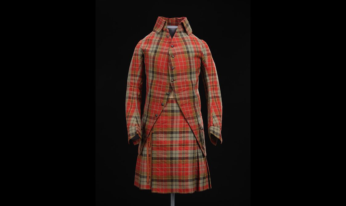 A mannequin wearing a red tartan kilt with a matching jacket with a high collar.