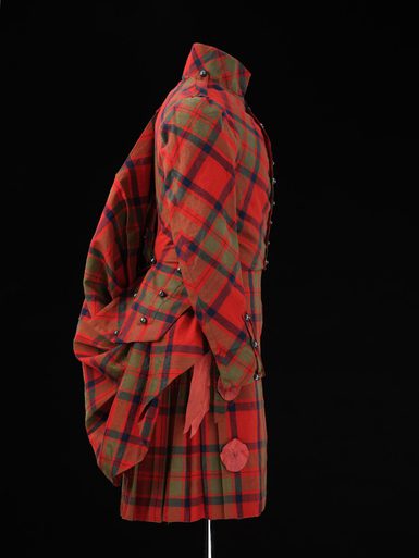 A side view of a mannequin wearing a red tartan kilt, jacket ,and shawl.
