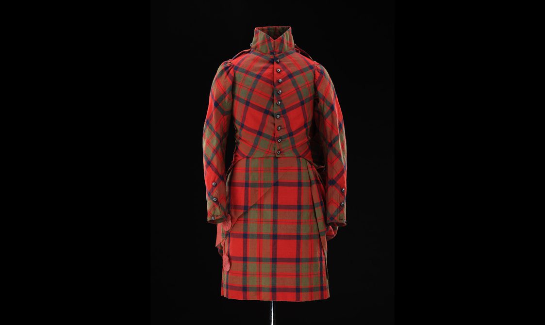 A mannequin wearing a red tartan kilt with a matching high collared jacket.