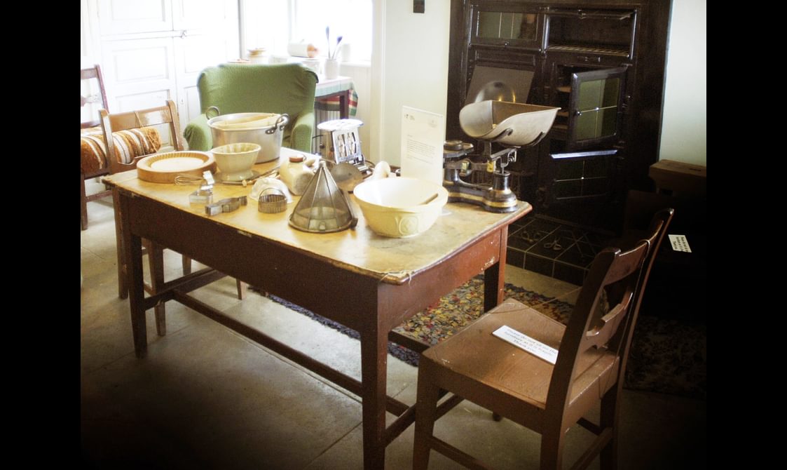 A room with 3 chairs and a wooden table. There are baking utensils on the top of the table.