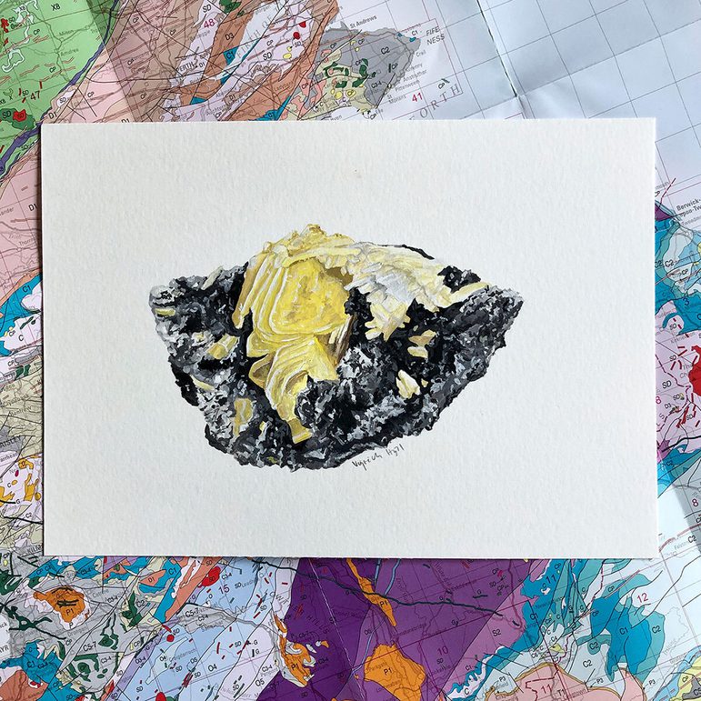 An illustration of a yellow mineral on a white piece of paper. The illustration is photographed against a geological map of Scotland.