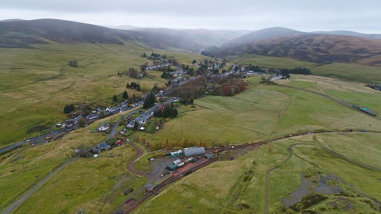 A photograph taken from above of a very small town among green land and hills