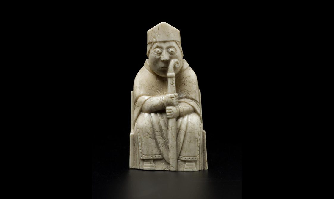 An ivory chess piece of a bishop seated wearing a pointed hat and holding a staff