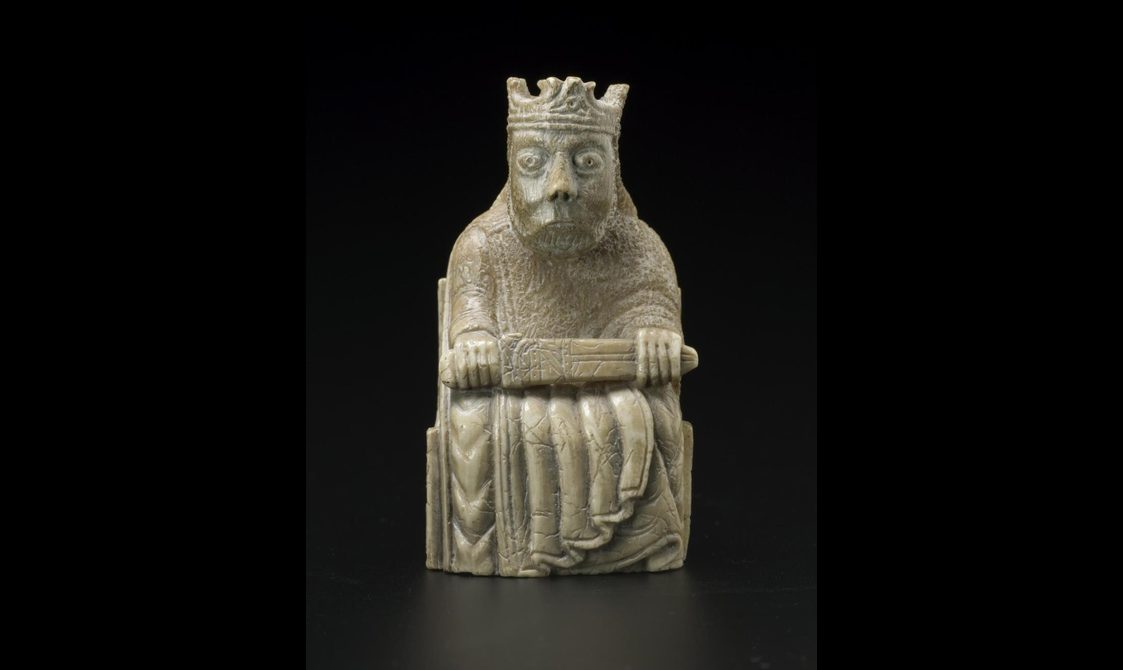 An ivory chess piece of a king seated with a crown on his head with a sword across his lap