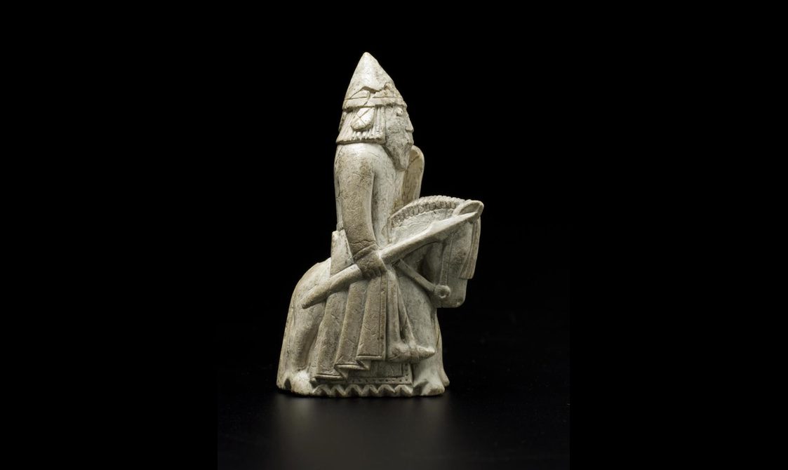 An ivory chess piece of a knight wearing a helmet and holding a spear while riding a horse