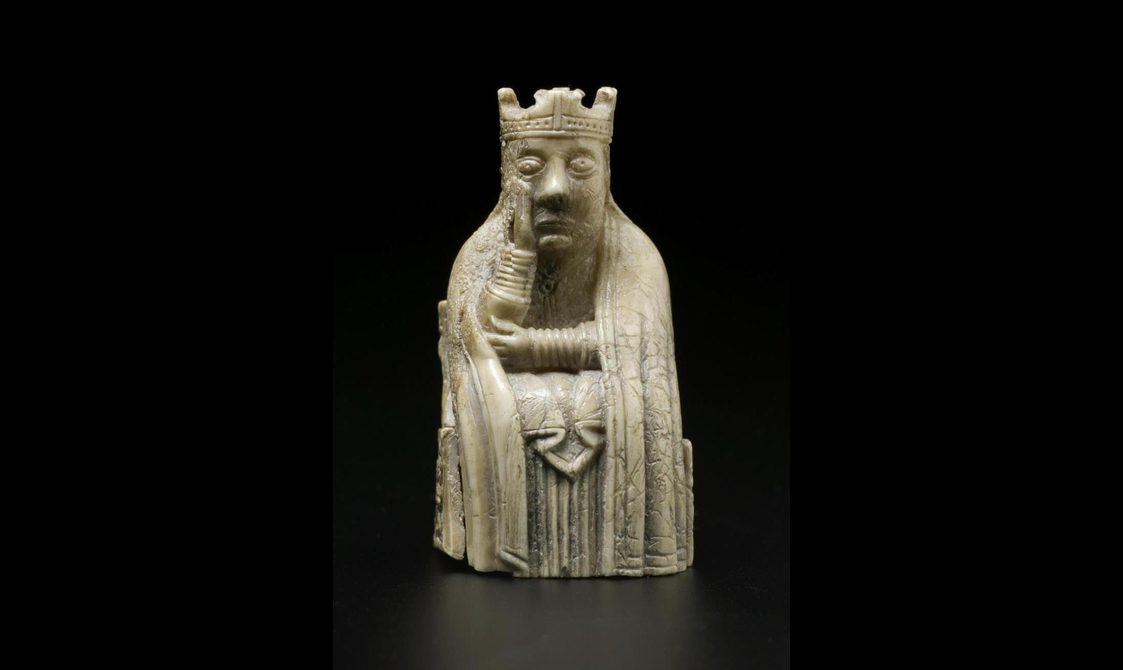 An ivory chess piece of a queen seated with a crown on her head with one hand cradling her face.