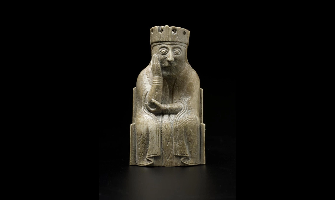 An ivory chess piece of a queen seated with a crown on her head with one hand cradling her face.