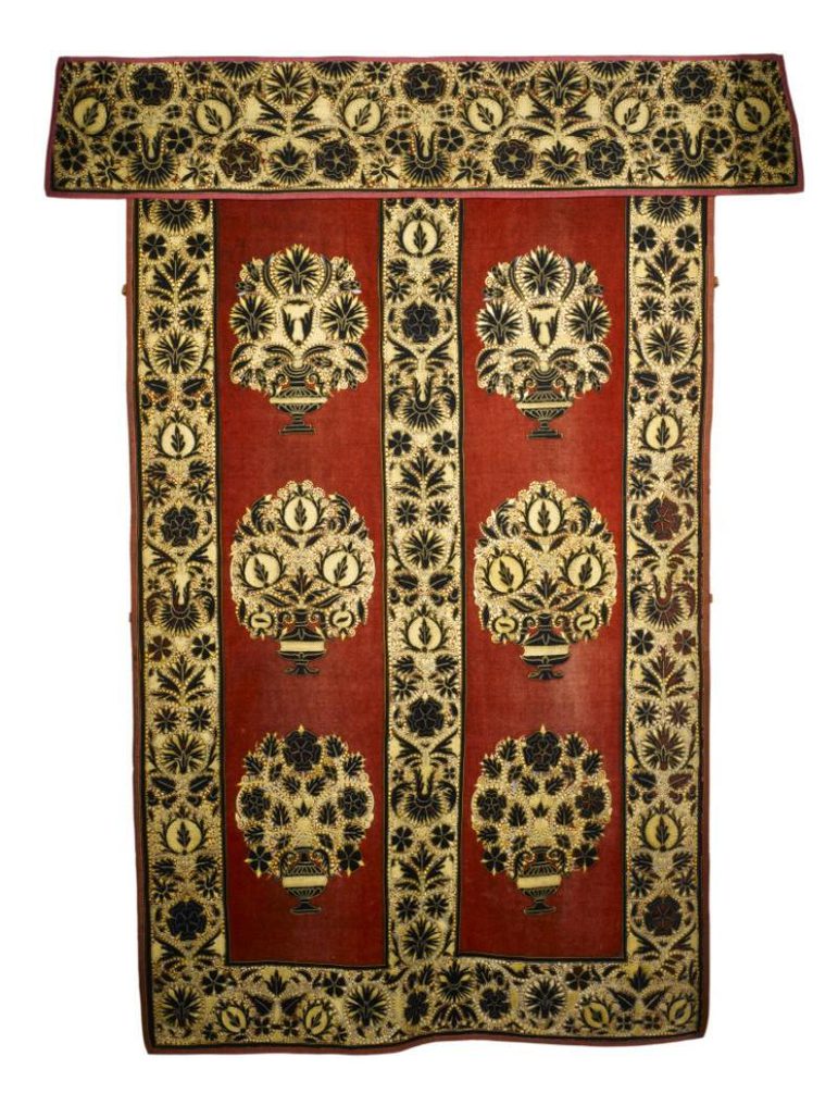 A gold and red wall hanging with intricate floral patterns around the border and in the middle.