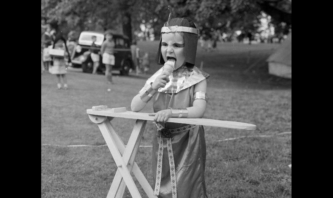A young boy in costume eats an ice cream in a field
