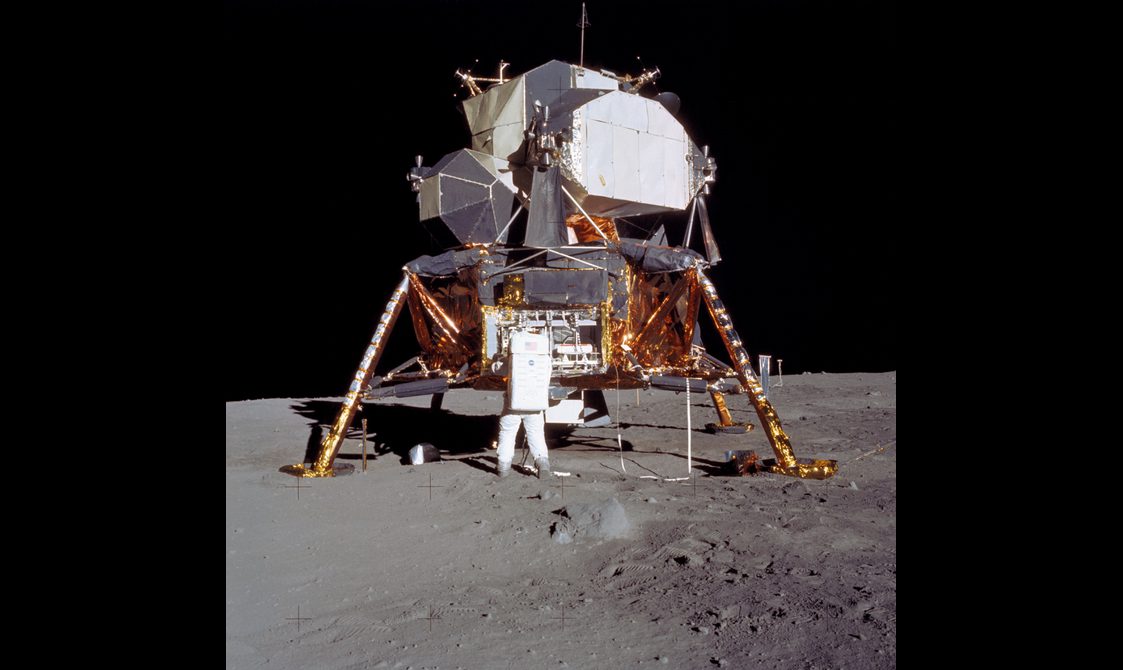 A large space craft sits on the moon with an astronaut working on the space craft.