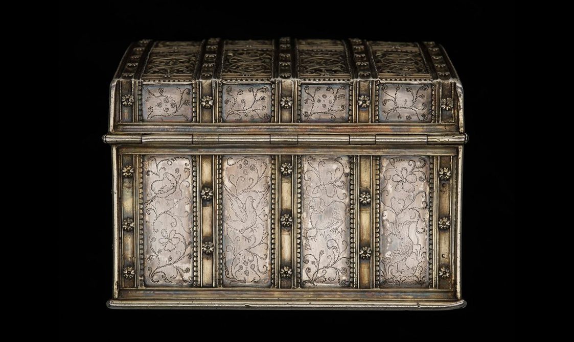 Side of the ribbon-like strap work silver casket decorated with flowers and pin pricked bird and branch motifs.