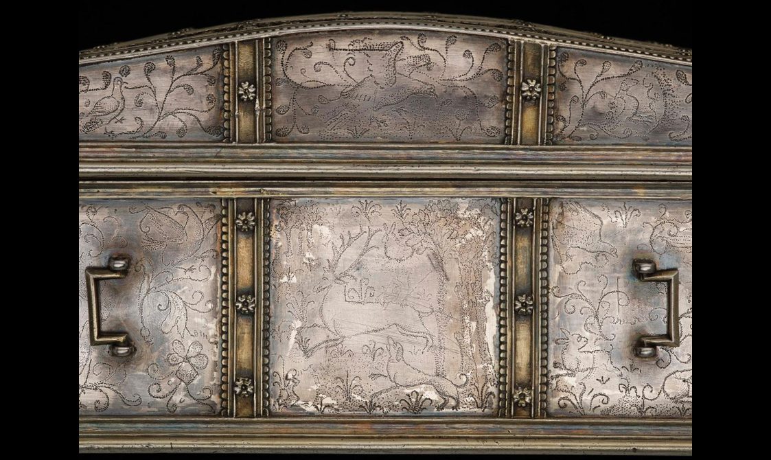 A close up of the ribbon-like strap work silver casket decorated with a stag, dog, bird and branch motifs.
