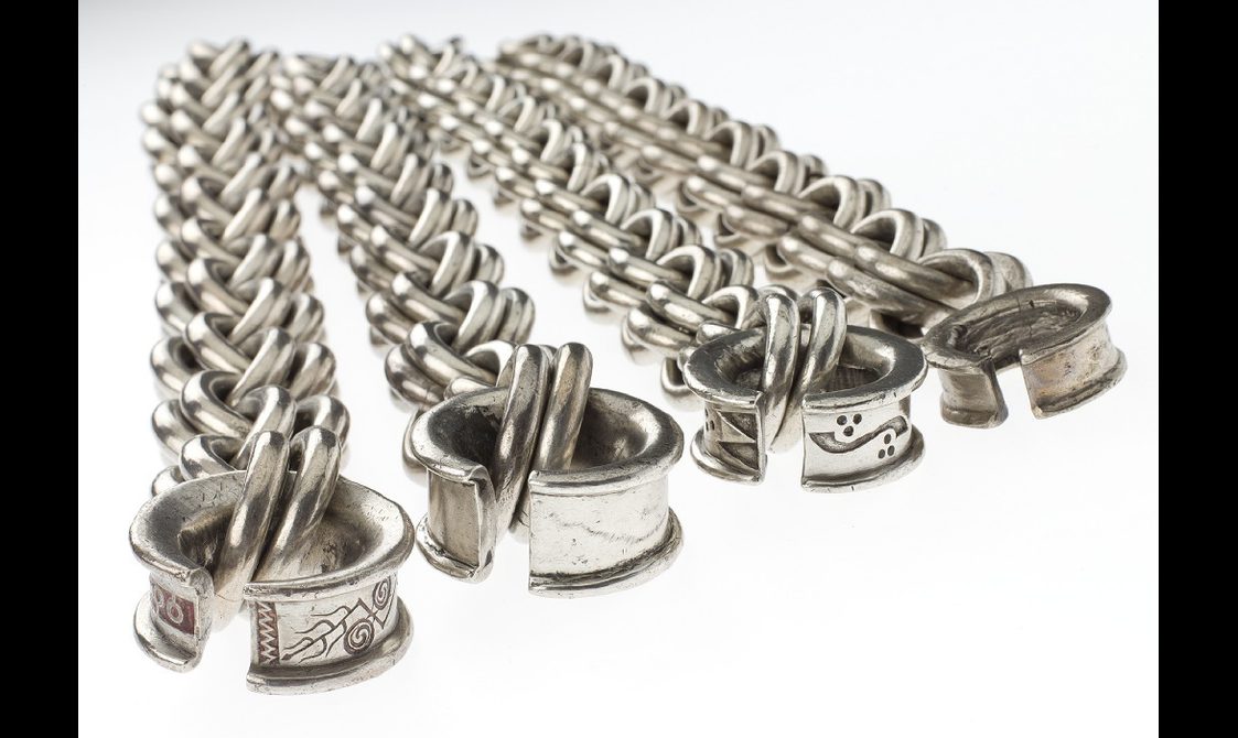 Four large horizontally laid silver chains with geometric and curve-shaped carvings