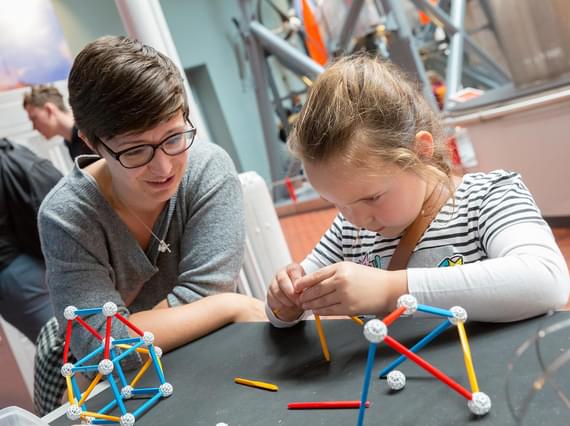 An adult and childing at a table building shapes with plastic sticks.