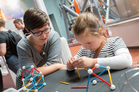 An adult and childing at a table building shapes with plastic sticks.