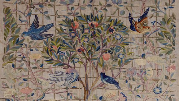A piece of embroidery artwork showing several colourful birds around a fruit tree.