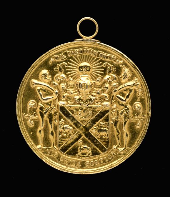 A gold circular medal with a coat of arms on its surface.