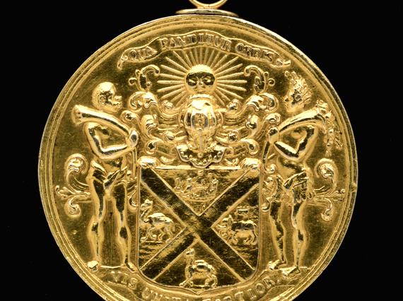 A gold circular medal with a coat of arms on its surface.
