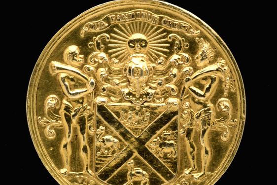 A gold circular medal with a coat of arms on its surface.