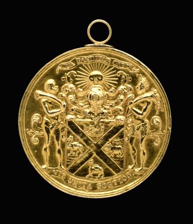 A gold circular medal with a coat of arms on its surface.