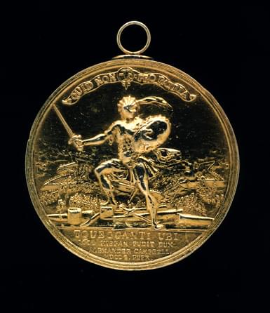 A gold circular medal with a coat of arms on its surface.