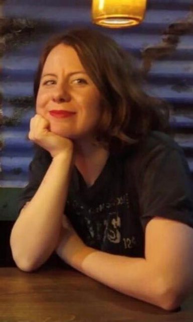A woman leaning against a table dressed in a dark T-shirt.