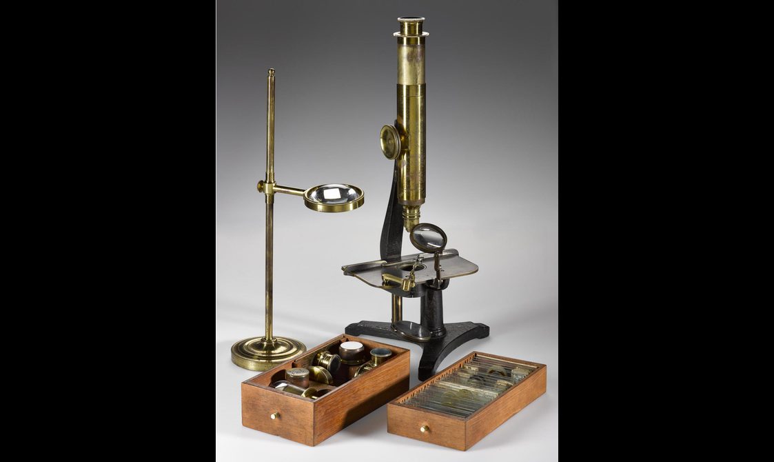 A brass microscope with wooden boxes containing sample slides and lens accessories.