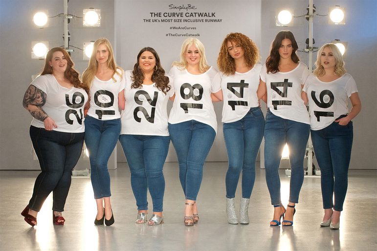 Seven women wearing blue jeans and white tshirts with numbers on them standing in a row with their arms around each other