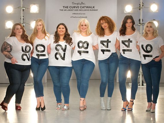 Seven women wearing blue jeans and white tshirts with numbers on them standing in a row with their arms around each other